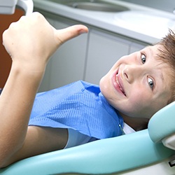 Young boy in dental chair giving thumbs up 